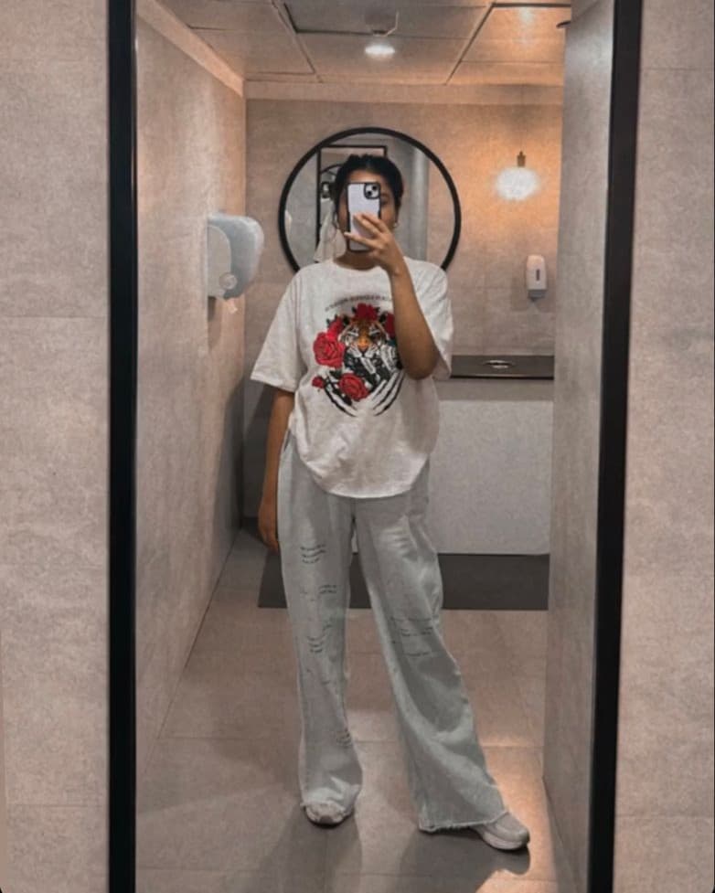 A mirror photo of a full outfit: an oversized printed white t-shirt, light distressed wide-leg jeans and white sneakers