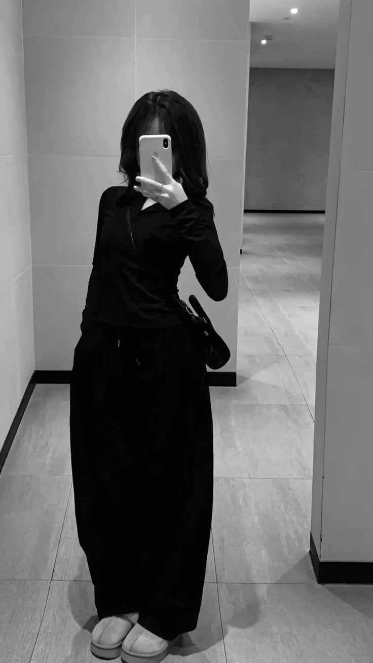 A black and white mirror selfie of a full-length outfit, a fitted long-sleeved top over a long skirt with platform slippers