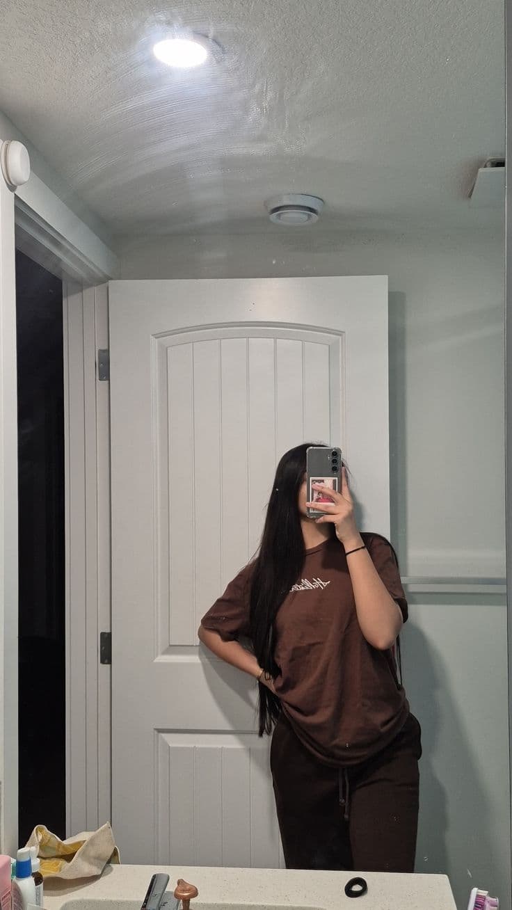 A mirror selfie taken in a bathroom where the frame is filled by ceiling and a door, the outfit is cut off at the thigh and the shoes are outside the shot