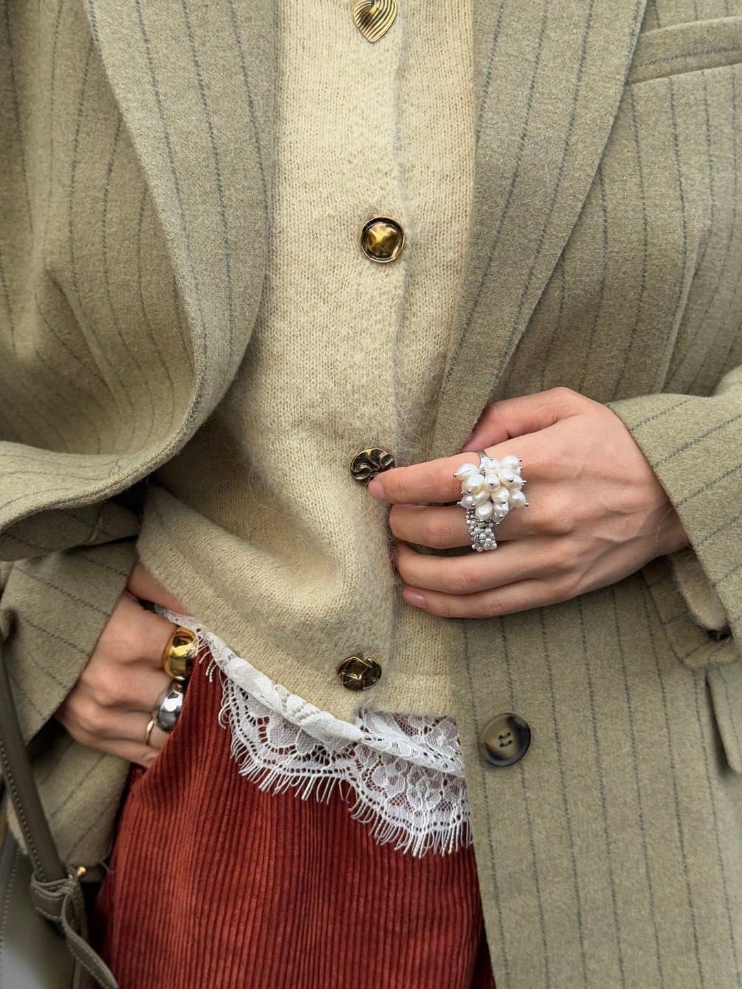 A close crop of a sage knitted cardigan fastened with gold dome buttons over a lace-trimmed slip and a rust corduroy skirt