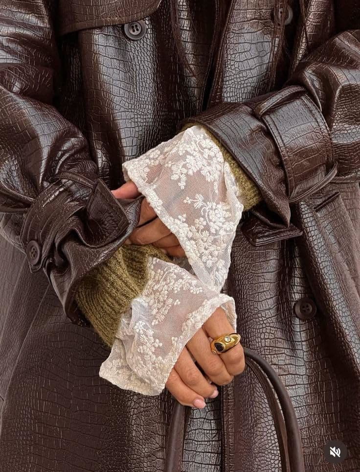 A close crop of a dark brown crocodile-effect leather coat cuff worn over a lace sleeve and an olive knit