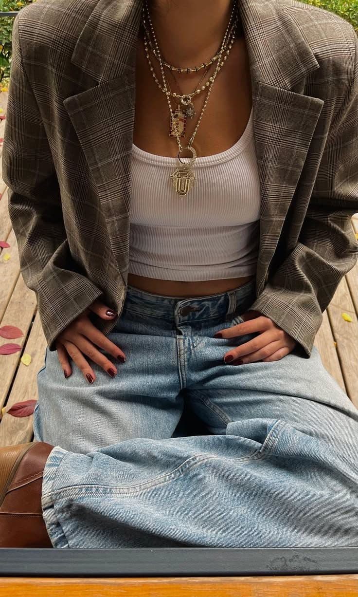 A cropped shot of an oversized brown checked blazer worn open over a white ribbed vest and light-wash wide-leg jeans