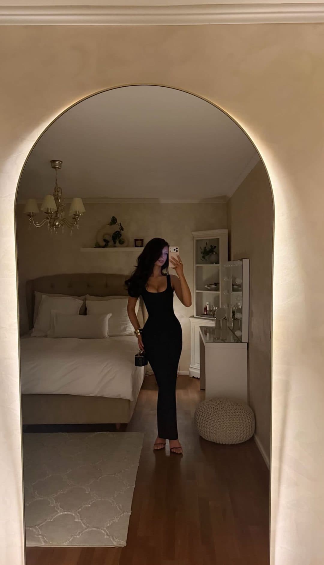 A vertical frame shot through an archway into a bedroom, with a woman in a long black dress standing small at the far end of the room