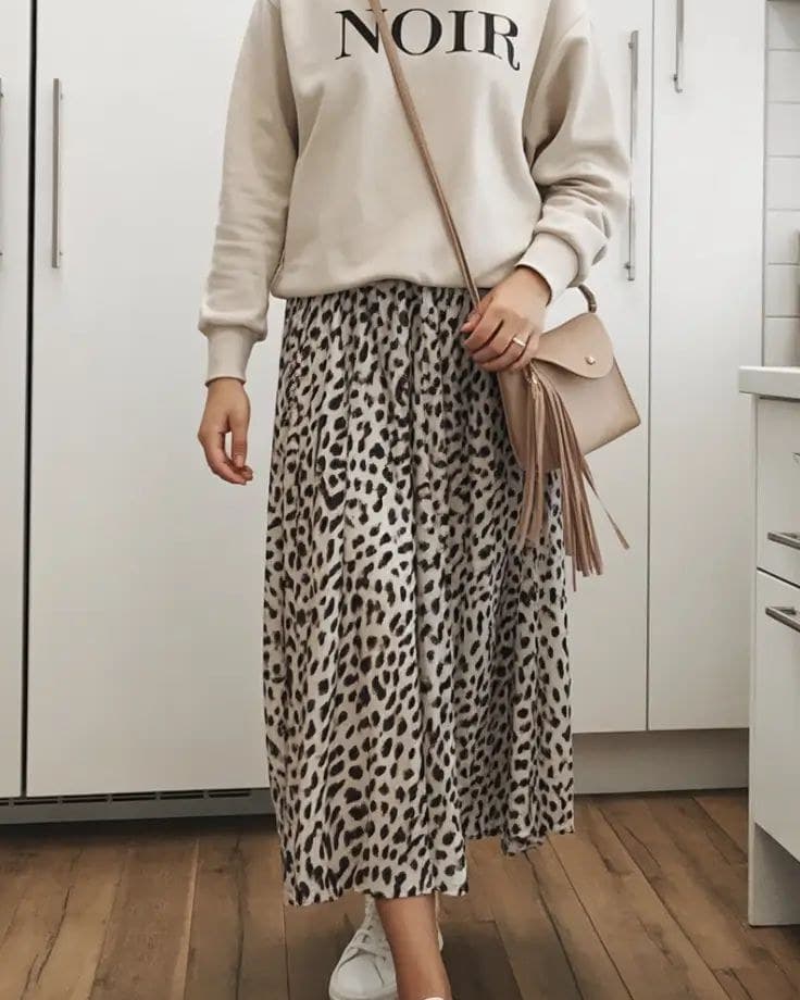 A pleated animal print midi skirt in bone and dark brown, worn with a cream graphic sweatshirt and a tan tasselled crossbody bag